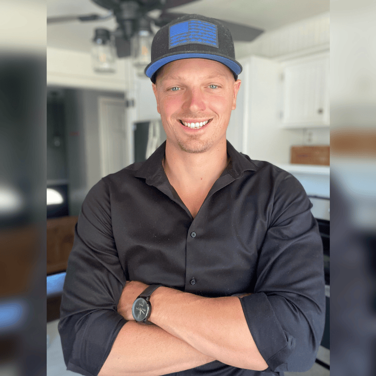 Smiling man wearing a black button-up shirt and a black-and-blue hat, with a blurred background